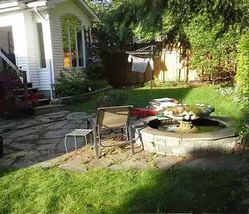 Overgrown backyard rebuilt with a natural stone patio — before